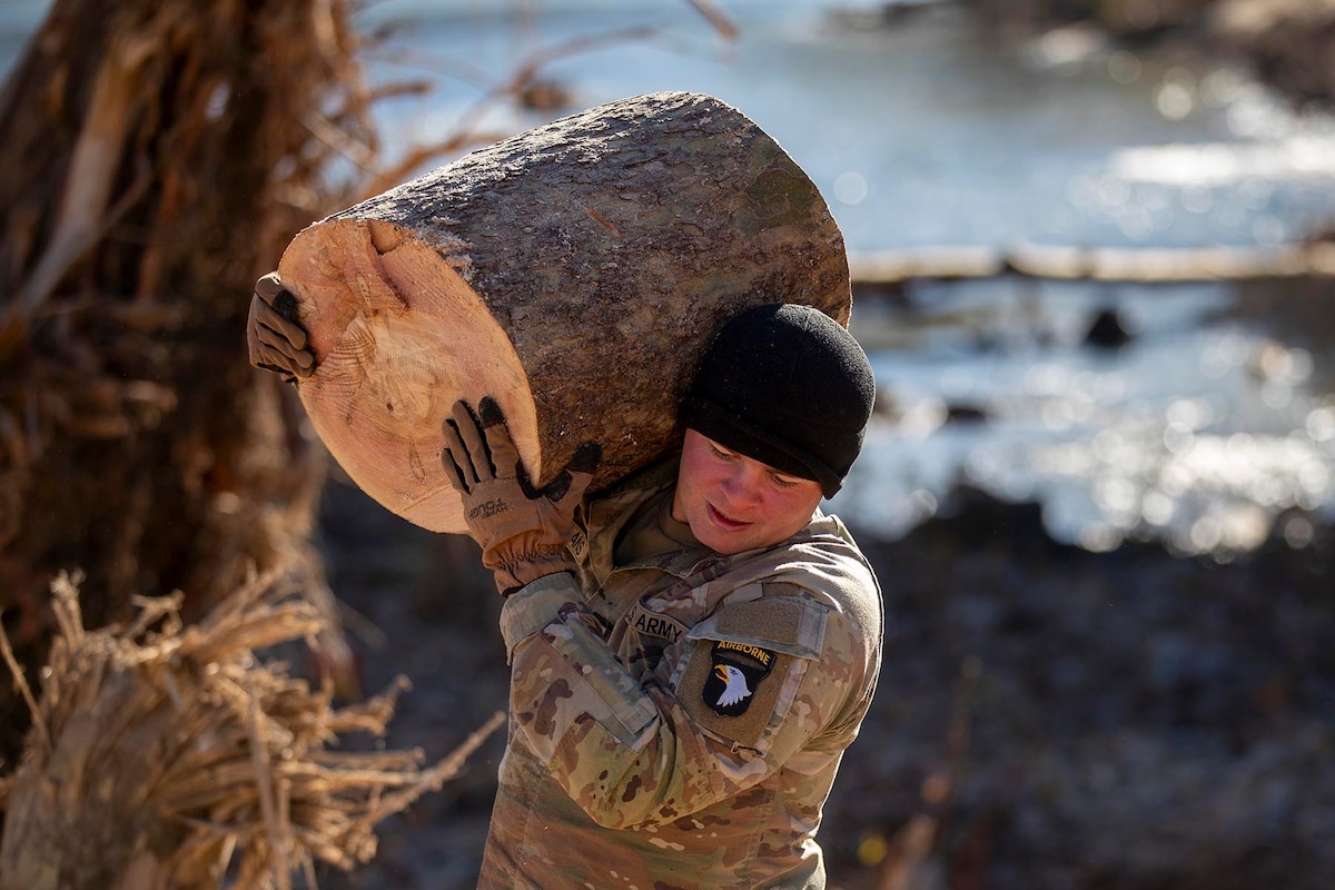 A soldier carries piece of trunk over his shoulder.