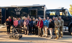 A group of people stand in front of a large blue truck that reads "USAF EOD", posing for a group photo outside on a fall day.