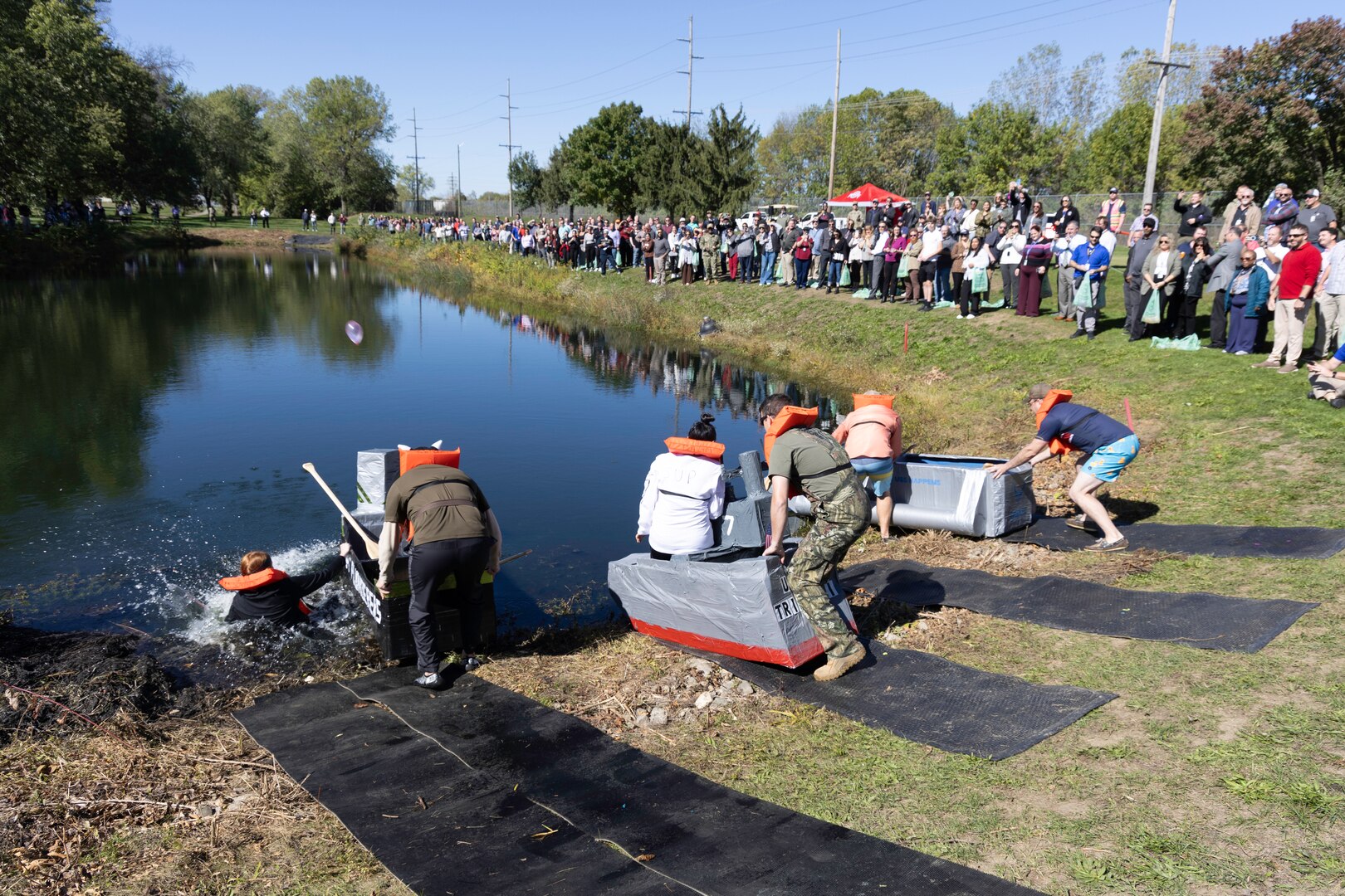 Cardboard boats get ready to launch from one side of a pond  outside.