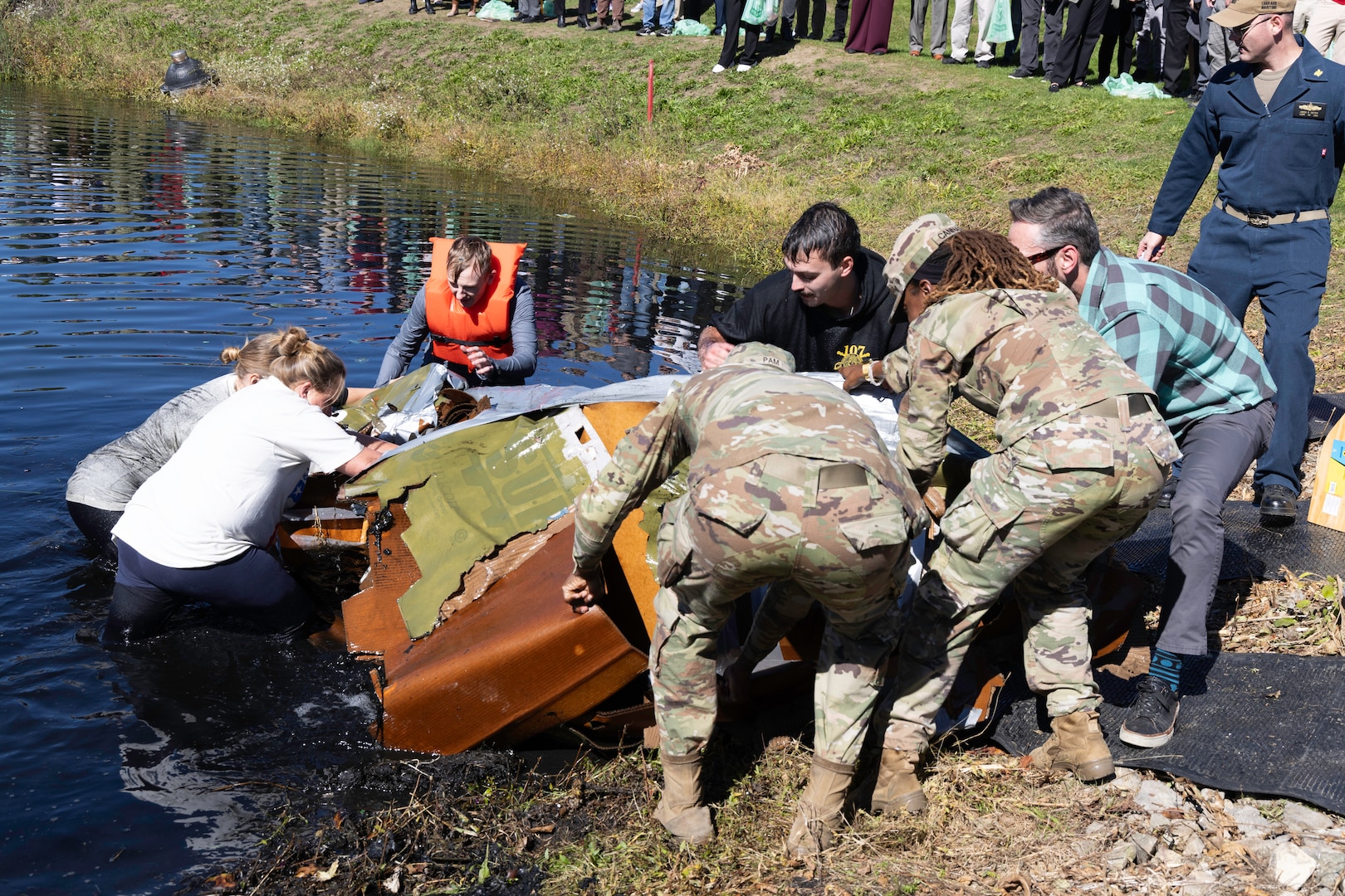 A large group of people pick up the remains of a cardboard boat which sank in a pond.