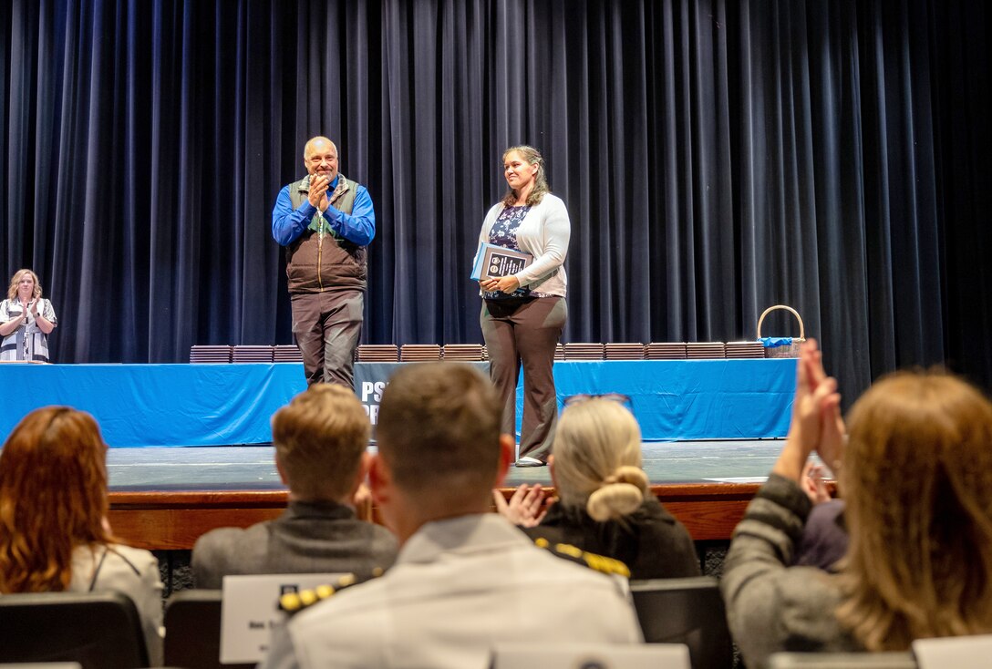Zanna Skirvin, machinist, Shop 31, Inside Machinist, receives the "Scholastic Award" from James Cappa, assistant production superintendent, Code 350, Inactive Fleet, Reactor Compartment Disposal and Recycling, during the 2024 Puget Sound Naval Shipyard & Intermediate Maintenance Facility Apprentice Program graduation ceremony, Sept. 20, 2024, at Bremerton High School in Bremerton, Washington. (U.S. Navy photo by Wendy Hallmark).