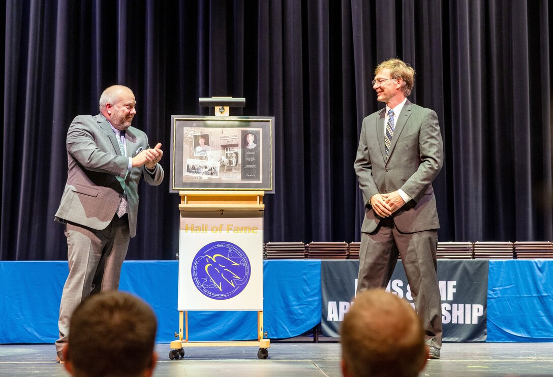 Rueben Farley, production training superintendent, Code 900T, Executive Development Program, presents the "Hall of Fame" plaque to retired Olympic College physics professor Bob Abel, in recognition of his lasting impact on the PSNS & IMF Apprentice Program, during the 2024 PSNS & IMF Apprentice Program graduation ceremony, Sept. 20, 2024, at Bremerton High School, in Bremerton, Washington. (U.S Navy Photo by Wendy Hallmark)
