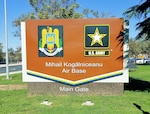 A sign featuring the Romanian air force emblem and US Army logo with the words Mihail Kogălniceanu Airbase Main Gate