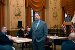 A man in a suit speaks to a room of people.
