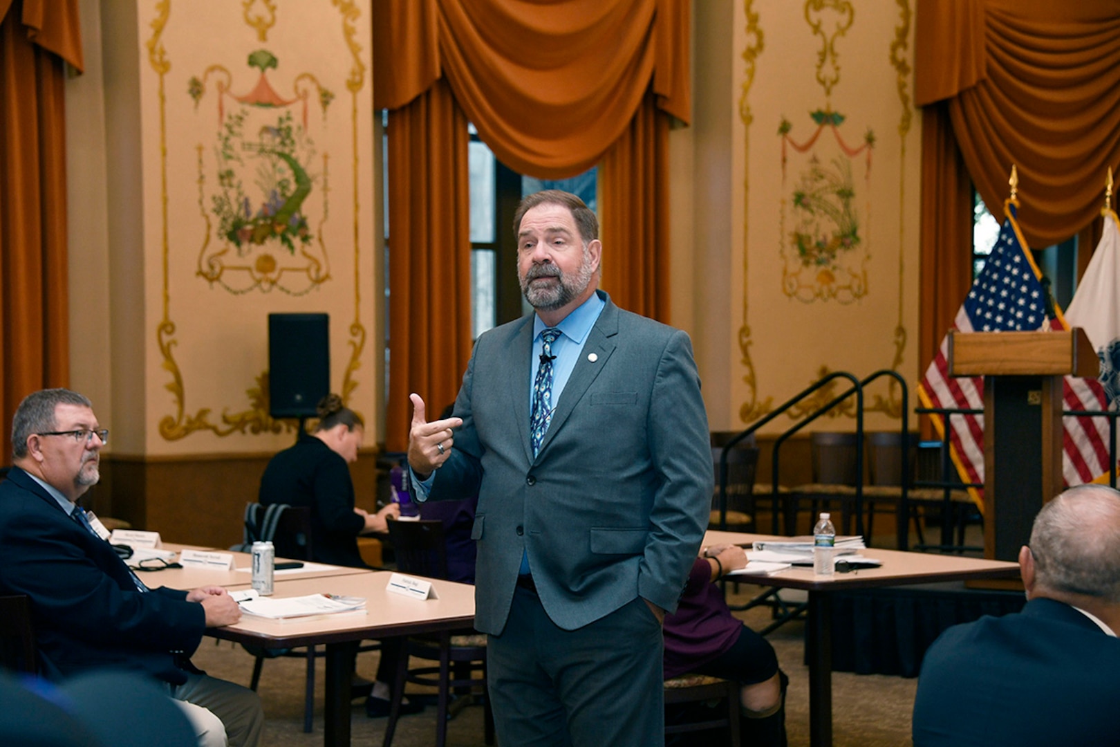 A man in a suit speaks to a room of people.
