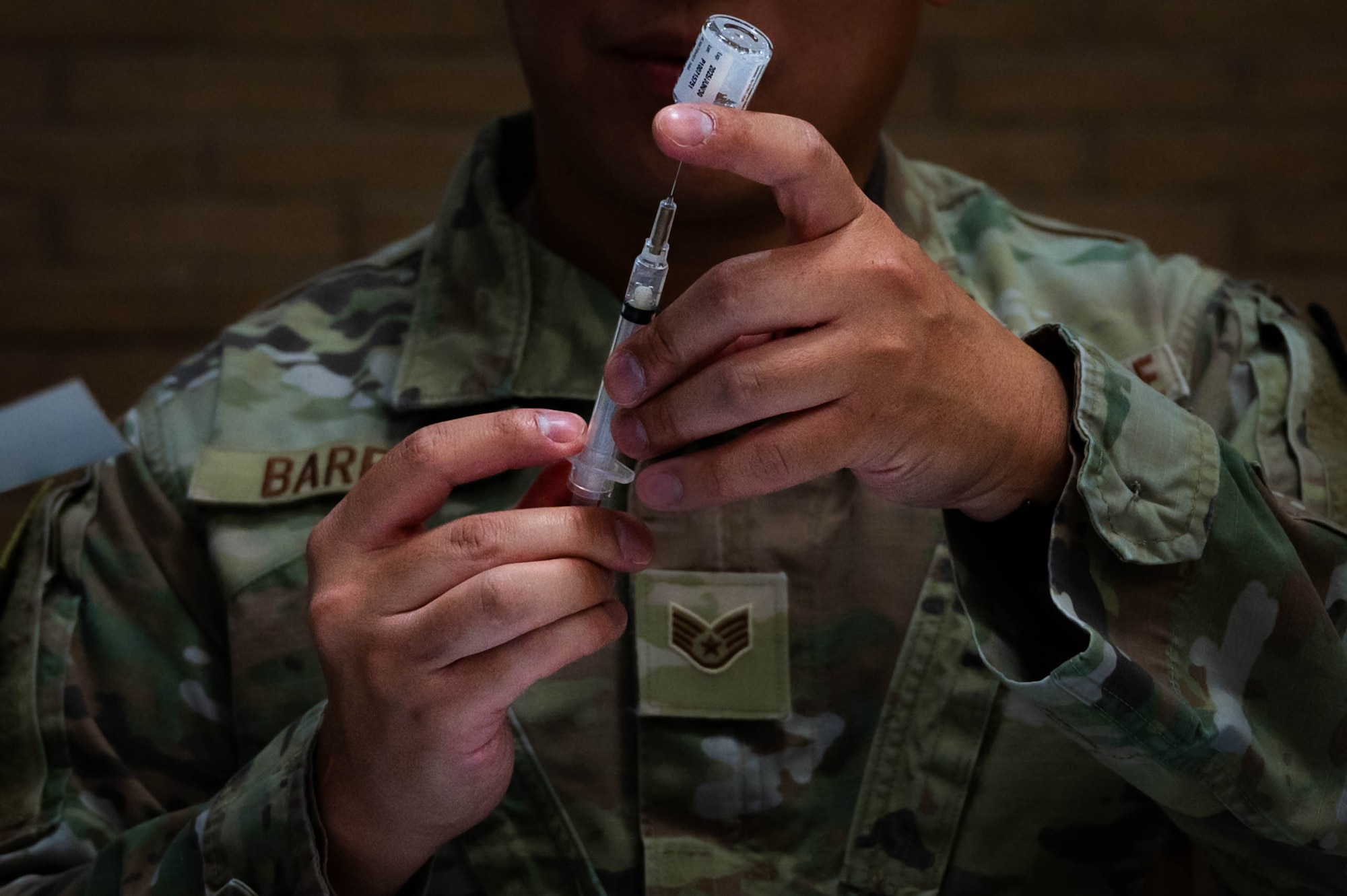 U.S. Air Force Staff Sgt. Mongeriq Barron, 56th Medical Group immunization technician, carefully draws liquid from a small glass vial into a syringe.