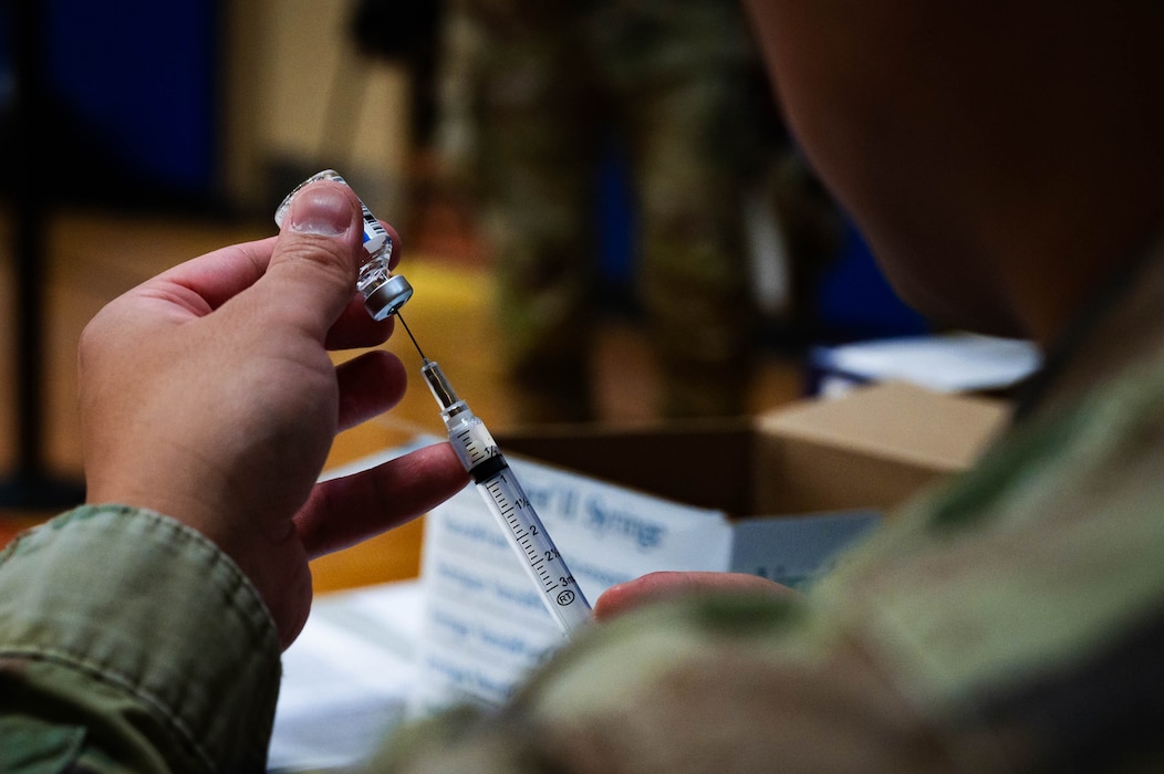 U.S. Air Force Staff Sgt. Mongeriq Barron, 56th Medical Group immunization technician, holds a syringe in one hand while gently inserting its needle into a small glass vial.