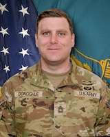 Man in U.S. Army uniform standing in front of two flags.