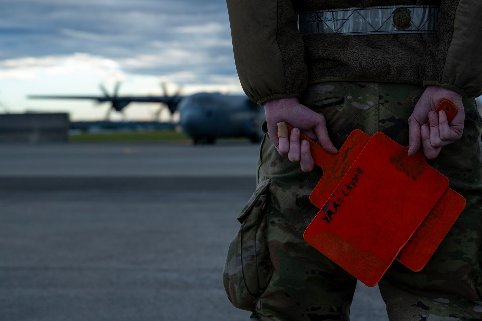 A military member holds orange marshalling paddles.