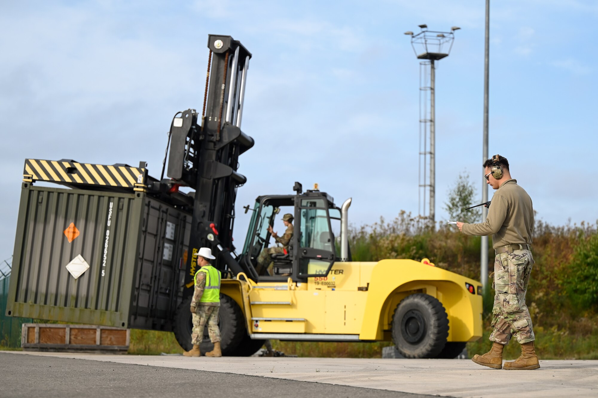 man reads shipping instructions and other airman drives forklift