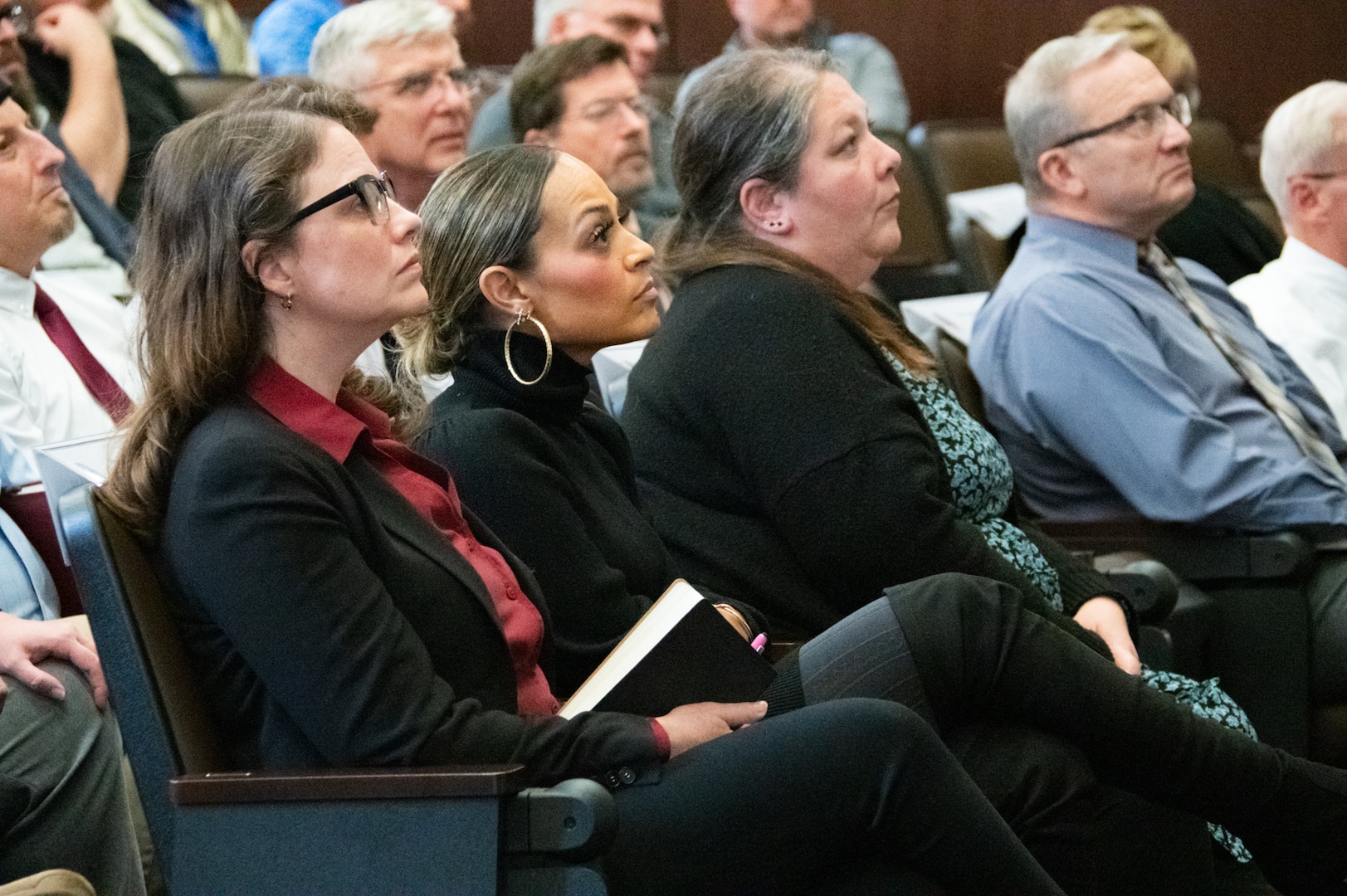 A group of people sit in an auditorium focused on a presenter.