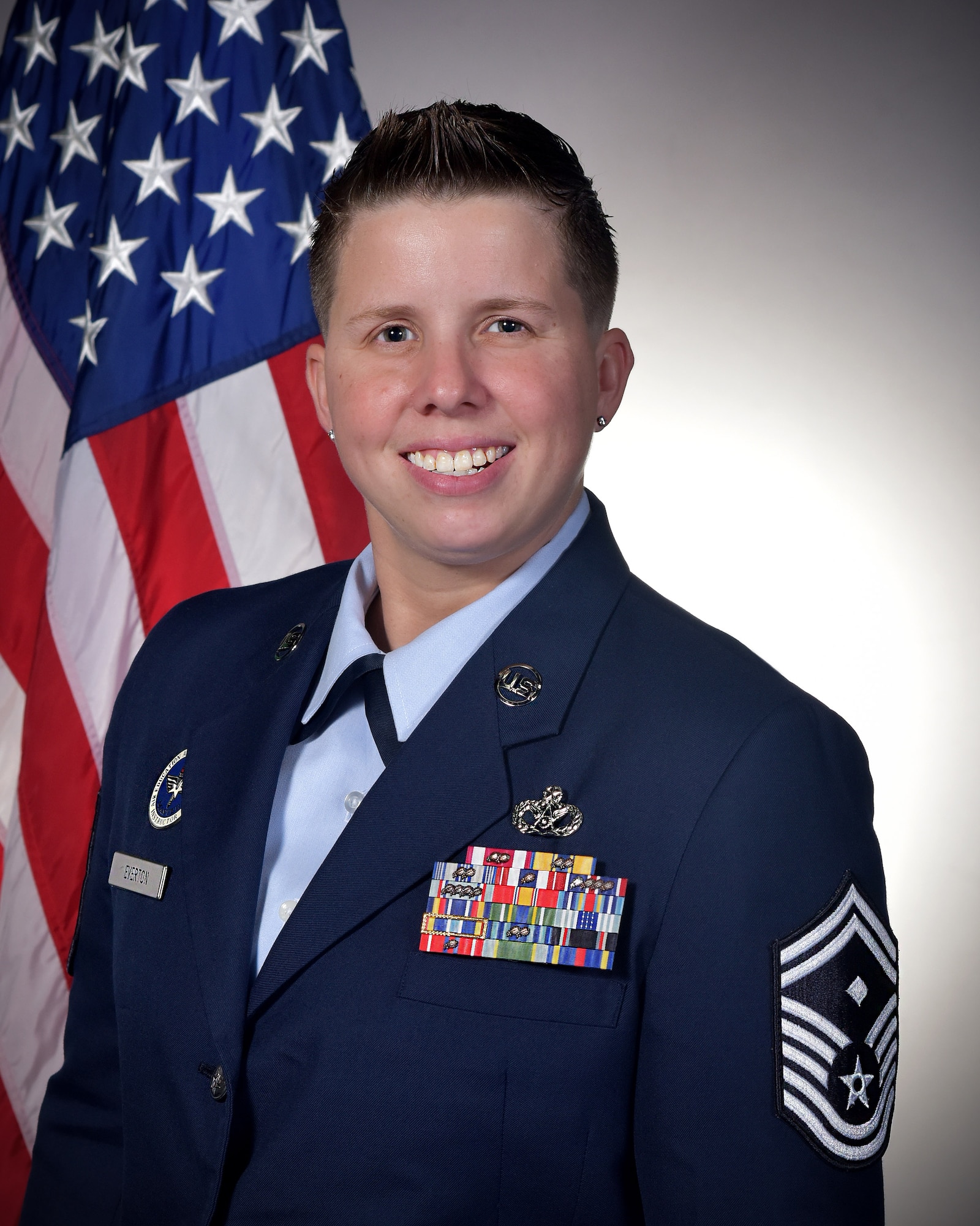 A woman in military dress blues poses next to an American flag.