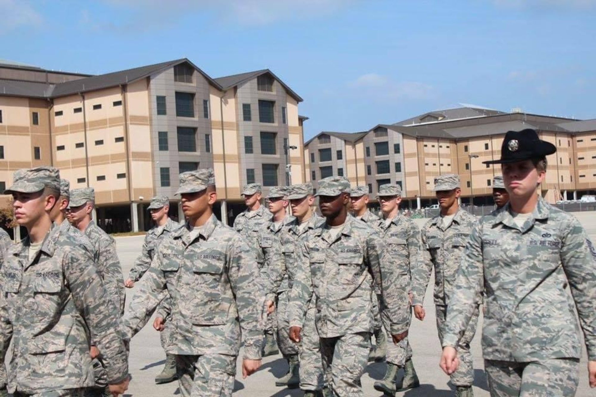 A woman walks alongside a group of Airmen; all are dressed in military uniforms.