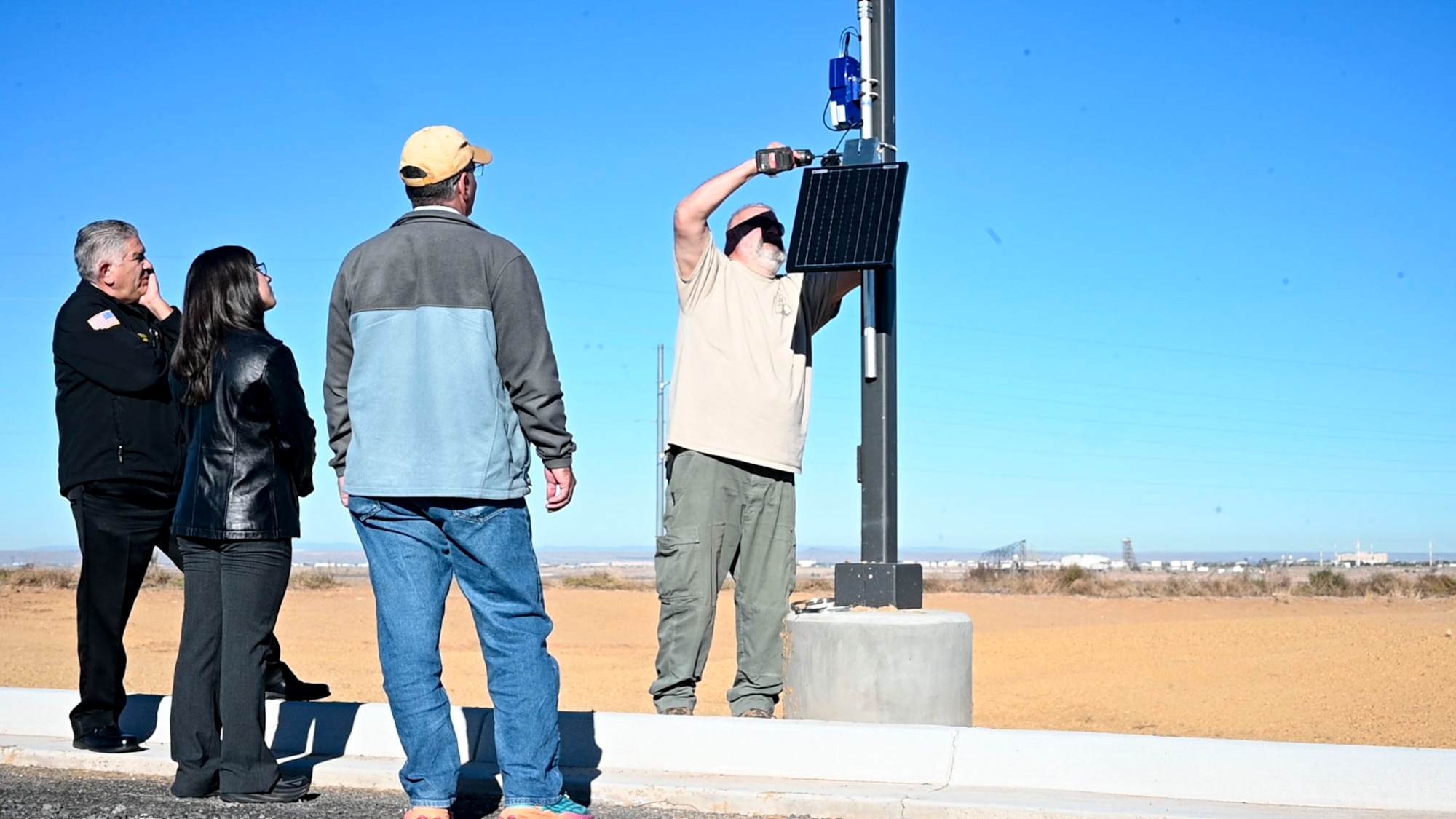 Man attaches wildfire sensor to post while three people watch