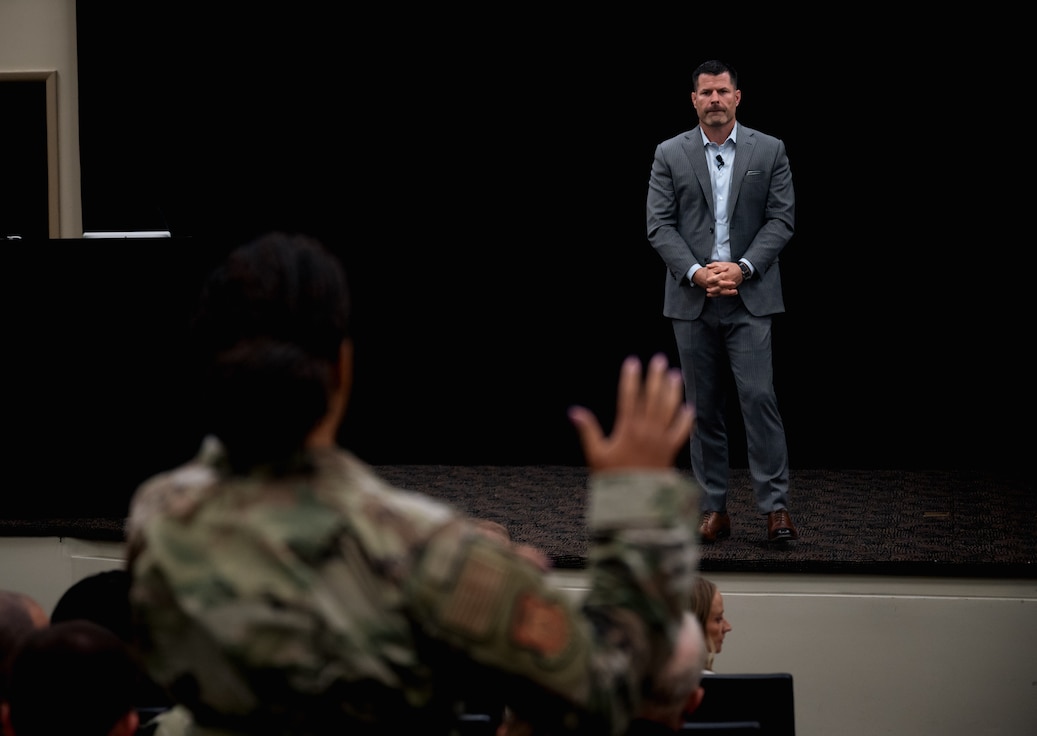 A man in a suit listens to a uniformed airman ask question