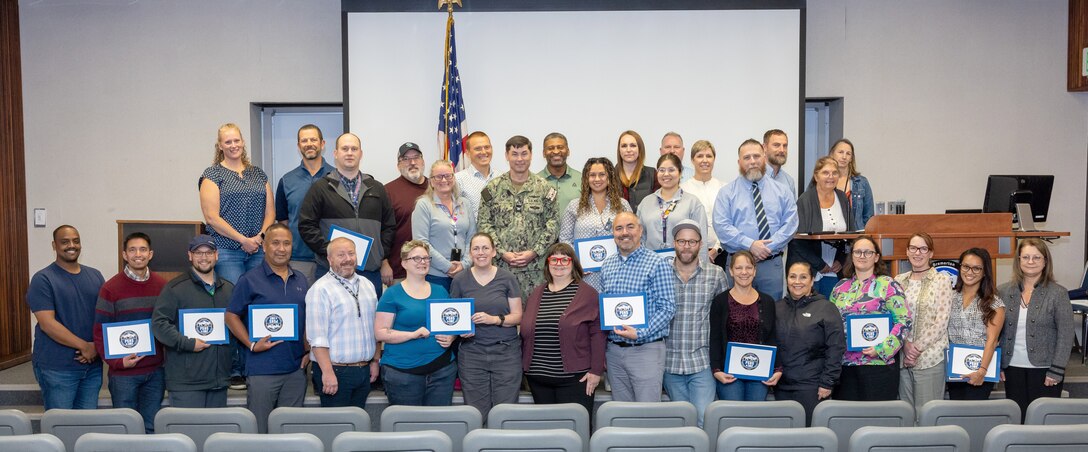 Capt. JD Crinklaw, commander, Puget Sound Naval Shipyard & Intermediate Maintenance Facility, poses for a portrait with Employee Resource Group award recipients, leaders, champions and supervisors, Oct. 8, 2024, following the annual PSNS & IMF ERG awards ceremony in the Shipyard Auditorium, in Bremerton, Washington. (U.S. Navy photo by Wendy Hallmark)