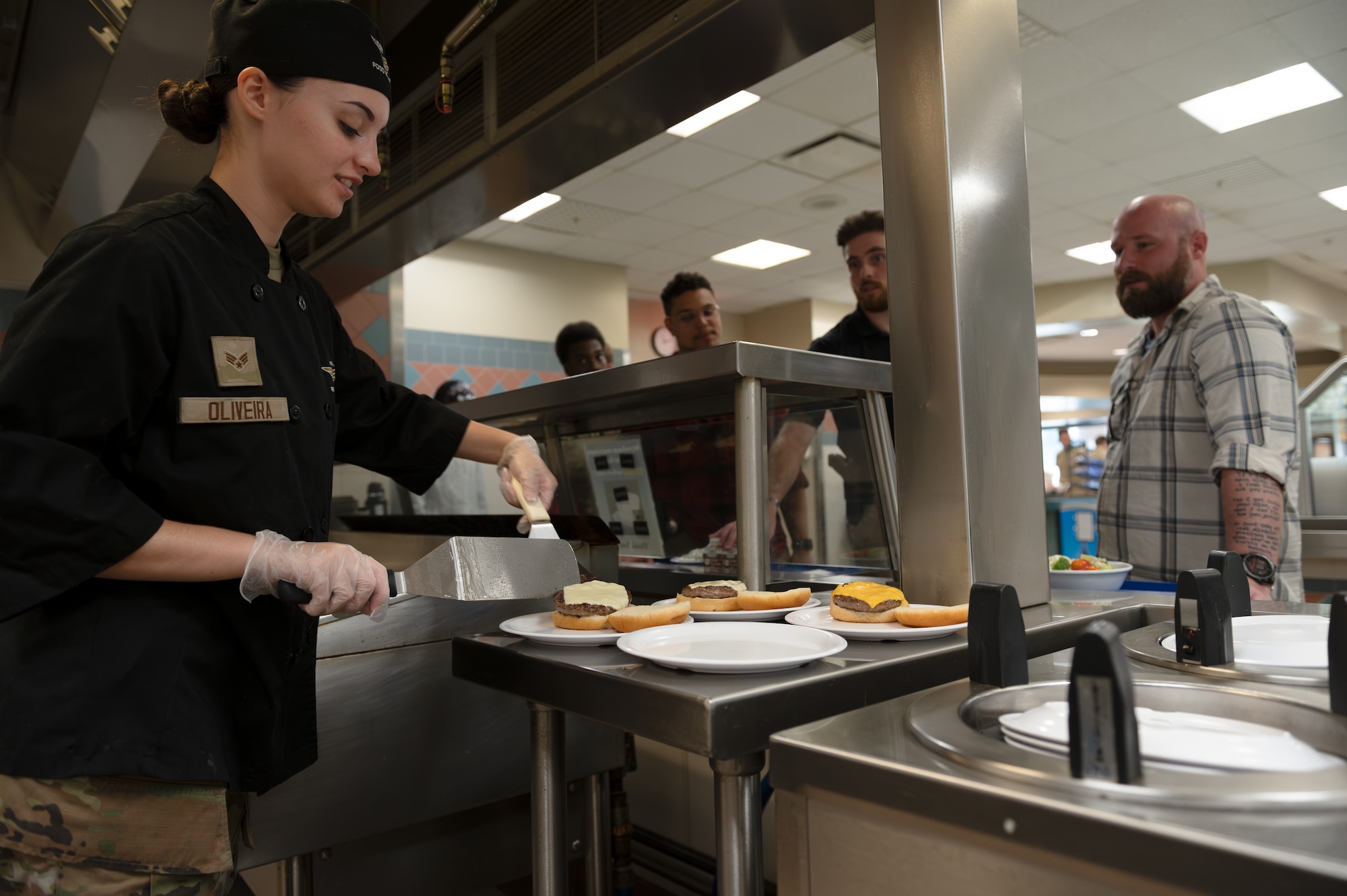 U.S. Air Force Senior Airman Shannon Oliveira, 1st Special Operations Force Support Squadron food service shift leader, places freshly cooked burgers onto plates at the Riptide Dining Facility on Hurlburt Field, Florida, Oct. 1, 2024.