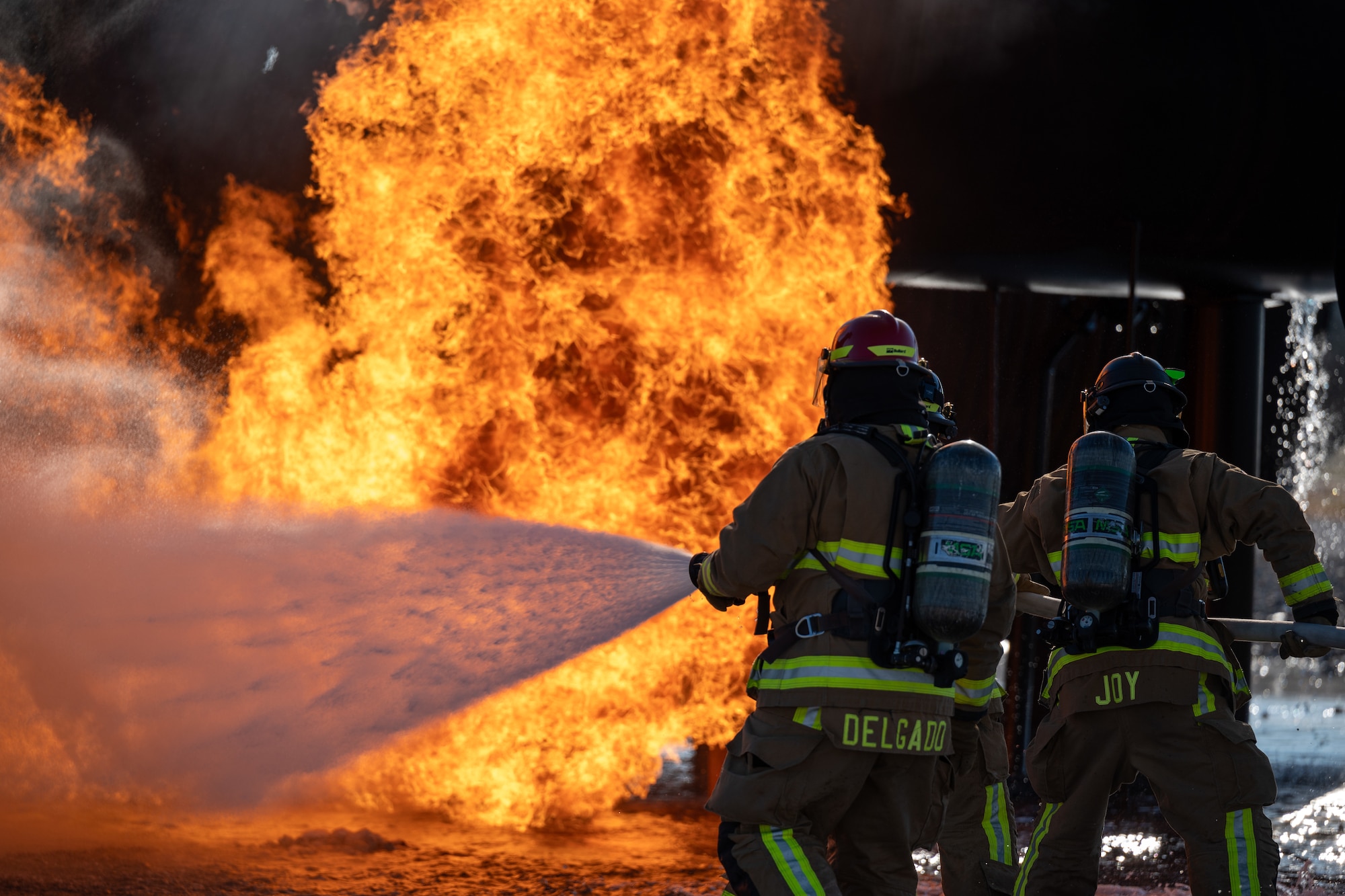 Firefighters from the 47th Civil Engineer Squadron spray water at the base of a fire during live fire simulations Laughlin Air Force Base, Texas, Oct. 15, 2024. Live fire simulations are valuable training opportunities for Airmen, allowing them to get advice on approach techniques, the order to put out fires and practice controlling a hose in uneven terrain. (U.S. Air Force photo by Staff Sgt. Nicholas Larsen)
