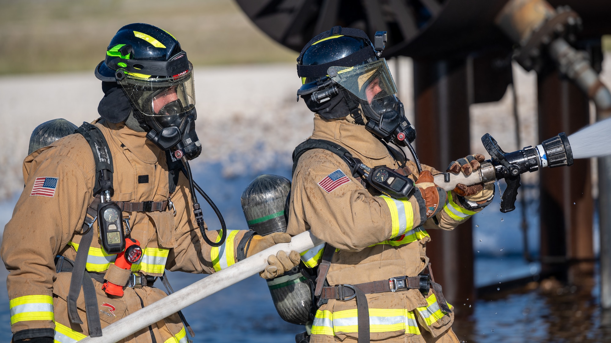 Firefighters from the 47th Civil Engineer Squadron spray water at an aircraft live fire simulator at Laughlin Air Force Base, Texas, Oct. 15, 2024. During the simulation, Firefighters used handlines to apply water to the fire pumping water from the tanker truck. (U.S. Air Force photo by Staff Sgt. Nicholas Larsen)