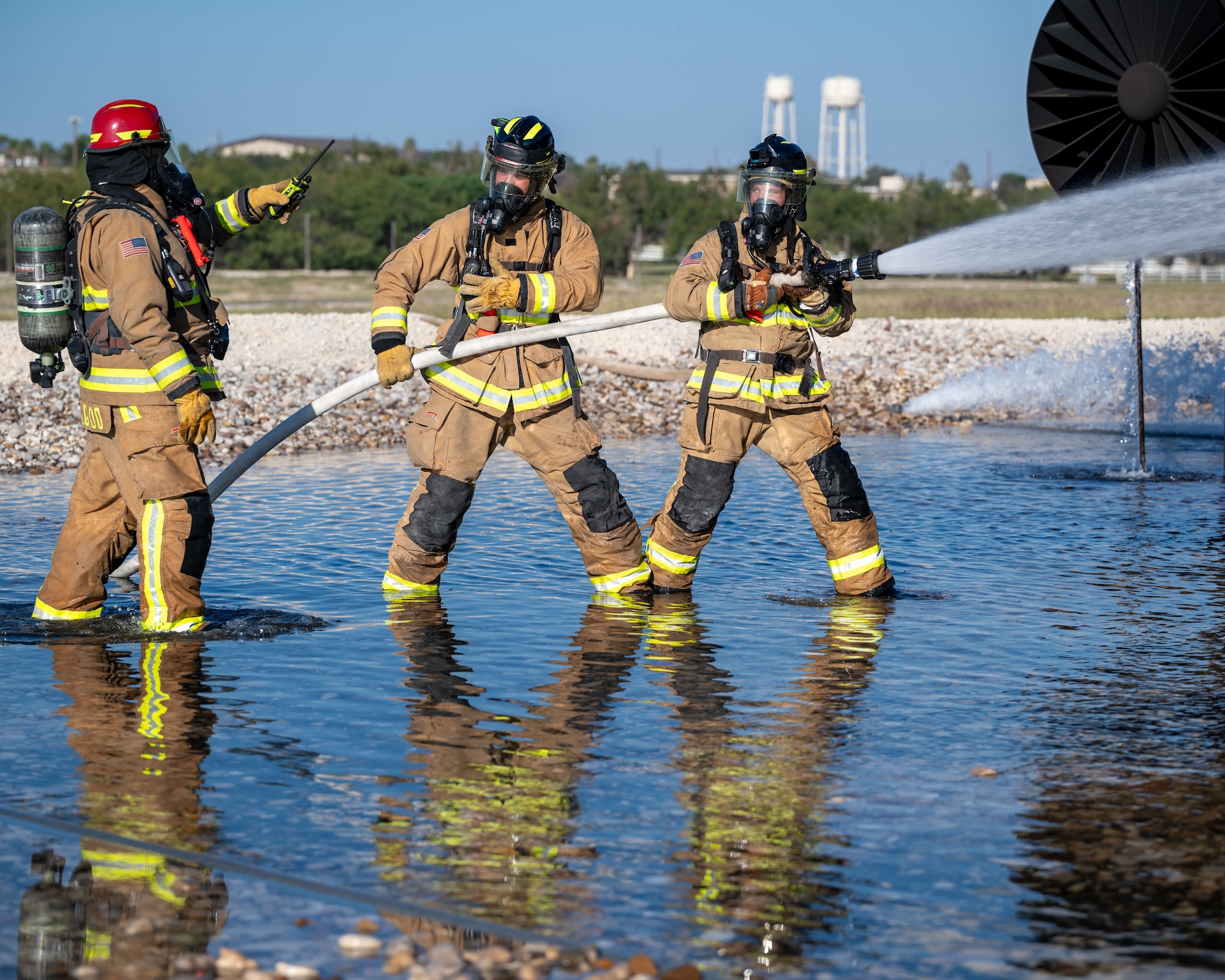 Firefighters from the 47th Civil Engineer Squadron receive additional instructions where to spray water at an aircraft live fire simulator at Laughlin Air Force Base, Texas, Oct. 15, 2024. During the simulation, Firefighters used handlines to apply water to the fire pumping water from the tanker truck. (U.S. Air Force photo by Staff Sgt. Nicholas Larsen)