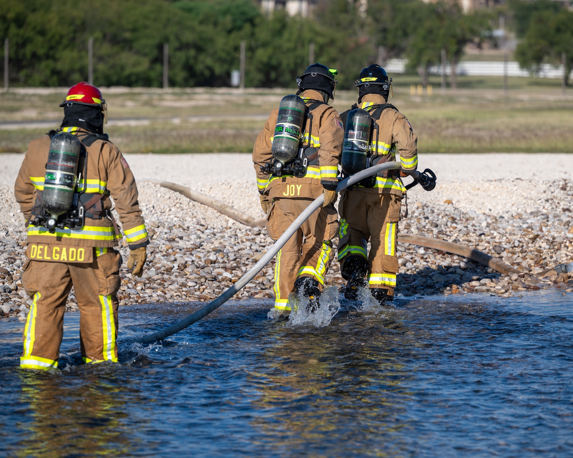 Firefighters from the 47th Civil Engineer Squadron move to fight a different area of the fire at an aircraft live fire simulator at Laughlin Air Force Base, Texas, Oct. 15, 2024. Firefighters need to maneuver around different parts of the simulator, taking care not to trip on rocks under the water. (U.S. Air Force photo by Staff Sgt. Nicholas Larsen)