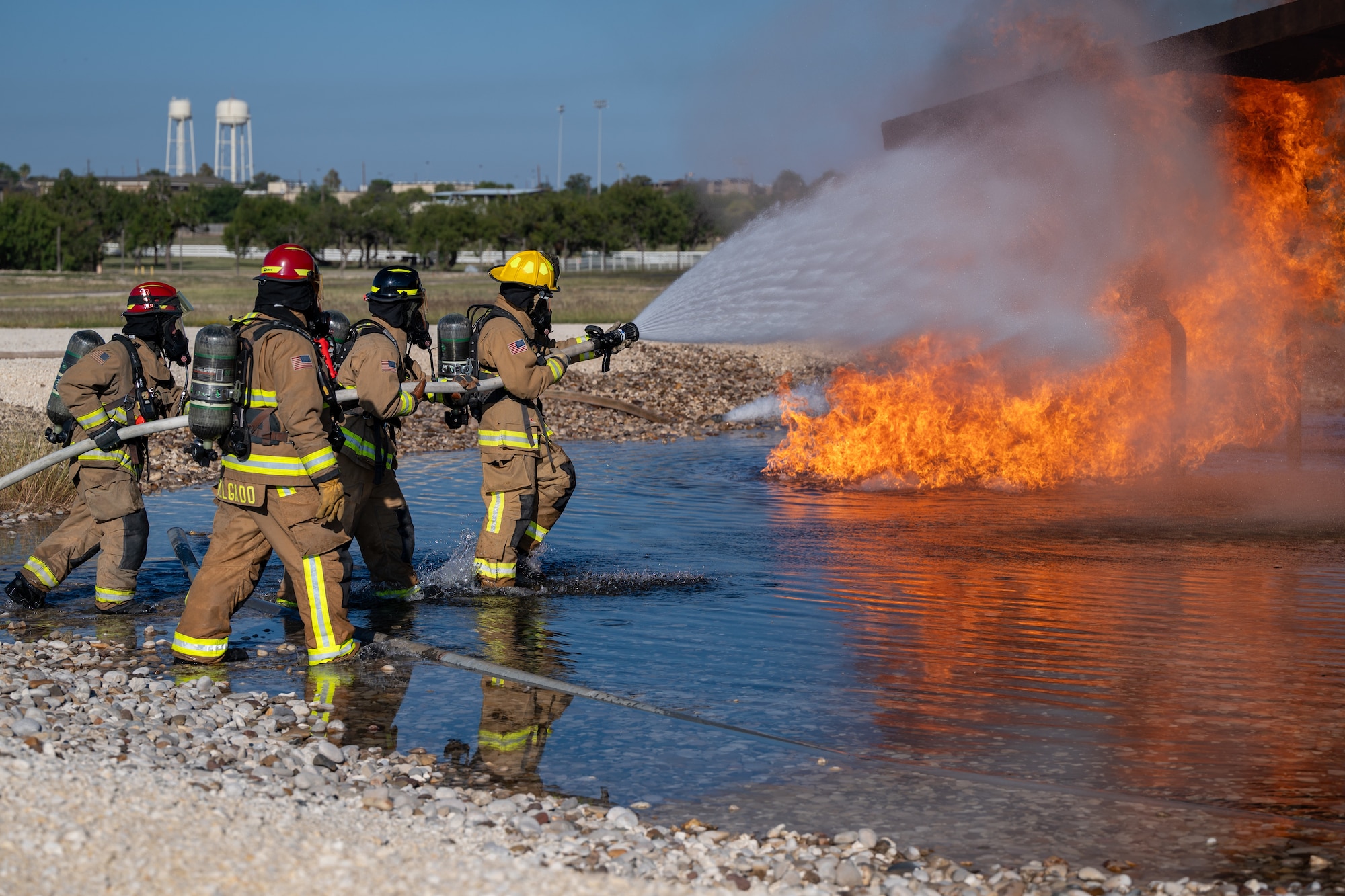 Firefighters from the 47th Civil Engineer Squadron spray water at a simulated engine cell on an aircraft live fire simulator at Laughlin Air Force Base, Texas, Oct. 15, 2024. When fighting the fire, the variable nozzle on the hose will be used to adjust how the stream of water lands on the fire, this can include a large cone of water to a tight jet to blast areas at further distances. (U.S. Air Force photo by Staff Sgt. Nicholas Larsen)