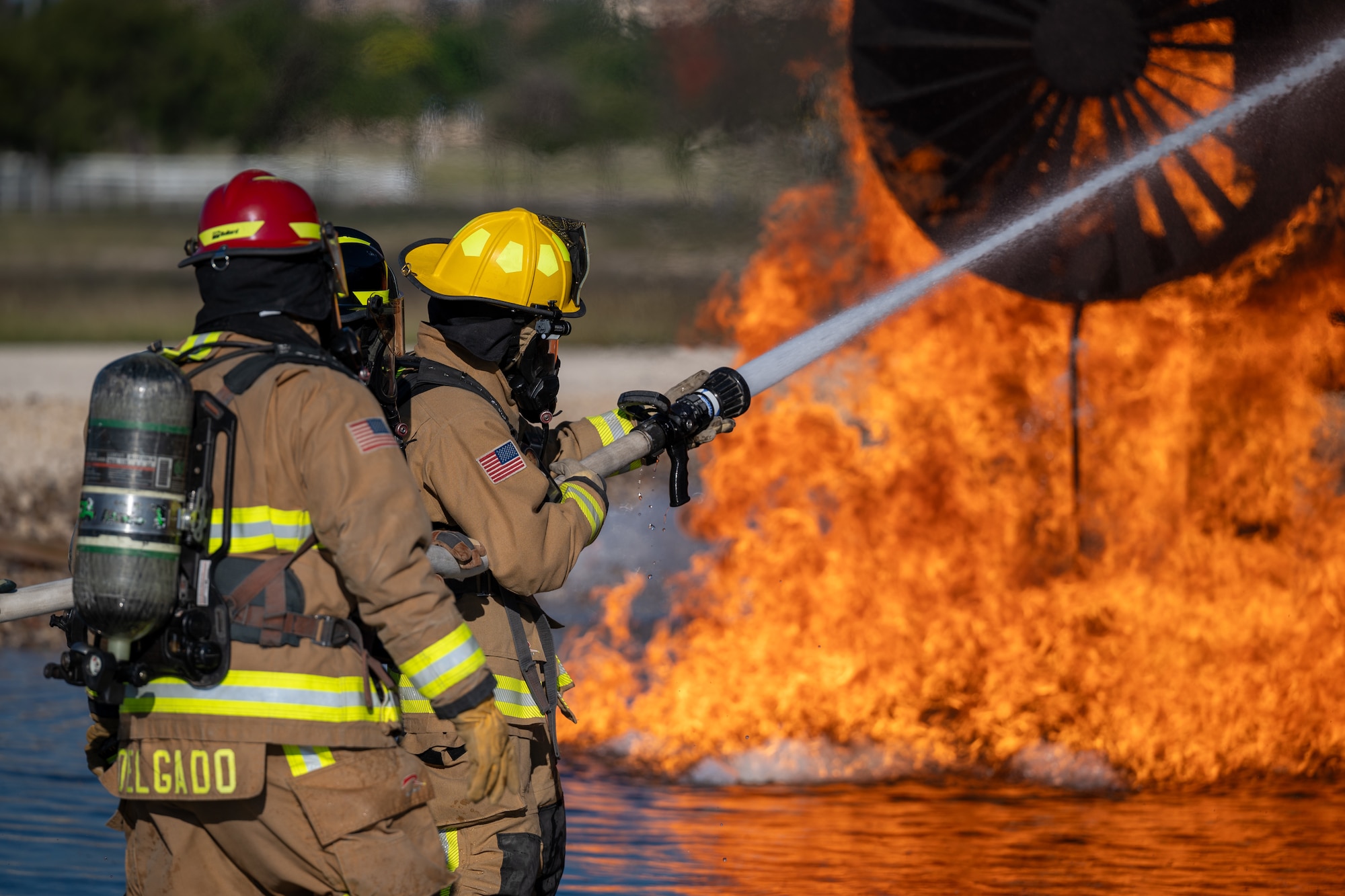 Firefighters from the 47th Civil Engineer Squadron spray water at a simulated engine cell on an aircraft live fire simulator at Laughlin Air Force Base, Texas, Oct. 15, 2024. When fighting the fire, the variable nozzle on the hose will be used to adjust how the stream of water lands on the fire, this can include a large cone of water to a tight jet to blast particular areas. (U.S. Air Force photo by Staff Sgt. Nicholas Larsen)