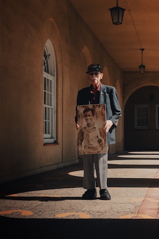Retired U.S. Marine Corps Maj. Billy Hall, a veteran of World War II, the Korean War, and Vietnam War, poses with a photo of his younger self when he was serving in WWII at Guadalcanal while standing on the Yellow Footprints at Marine Corps Recruit Depot San Diego, California, Oct. 11, 2024. Hall visited MCRD San Diego to attend a graduation ceremony for Bravo Company, 1st Recruit Training Battalion. The Yellow Footprints are iconic to the Depot as all recruits stand upon them to receive initial instruction during their immediate arrival for training to become Marines. (U.S. Marine Corps photo by Cpl. Alexander O. Devereux)