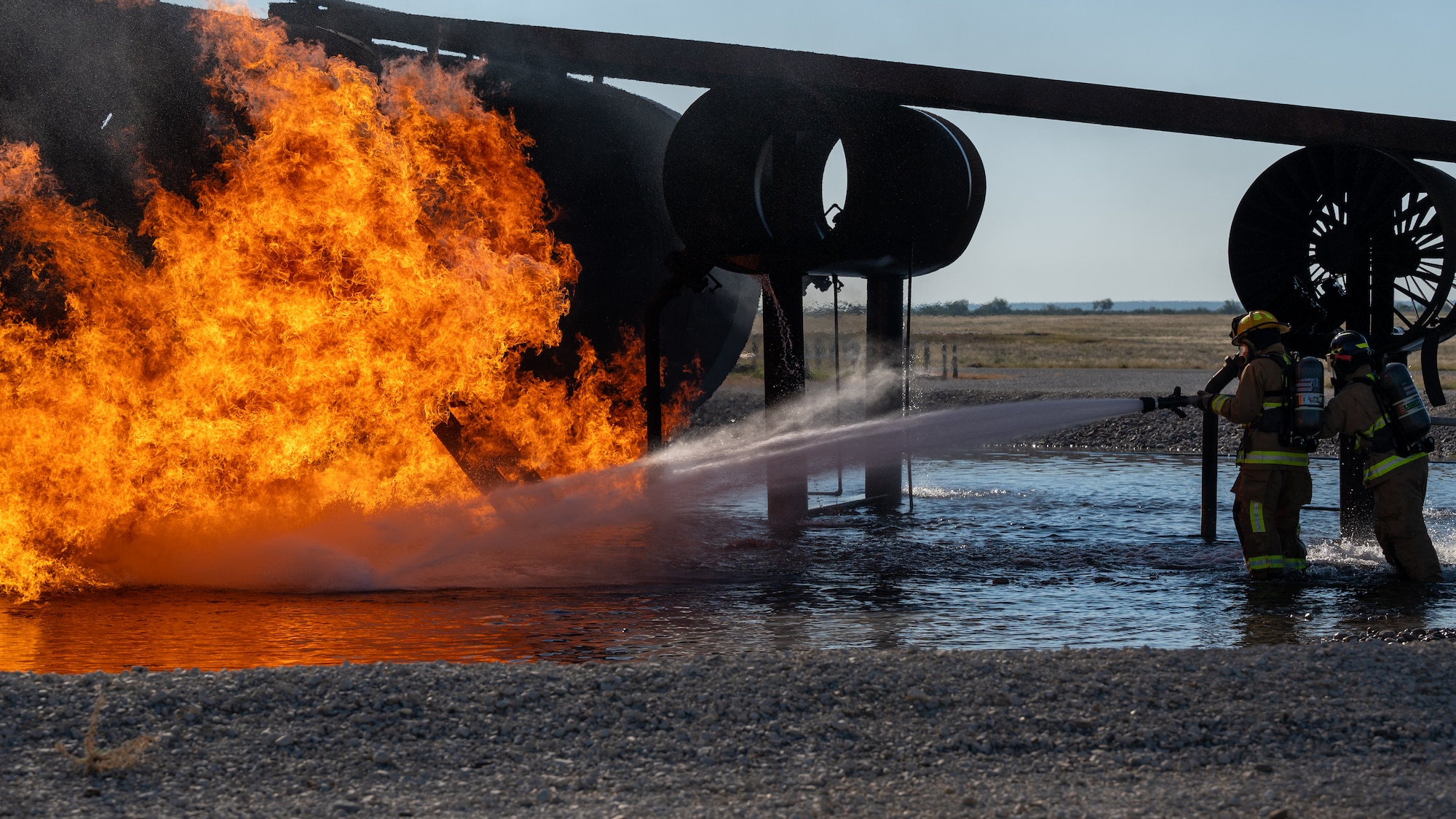 Firefighters from the 47th Civil Engineer Squadron spray water at a fire on the fuselage of an aircraft live fire simulator at Laughlin Air Force Base, Texas, Oct. 15, 2024. Fighting fires in a simulator provides a controlled area for firefighters to hone their skills while dealing with the real stressors of heat, flames and the use of real equipment. (U.S. Air Force photo by Staff Sgt. Nicholas Larsen)