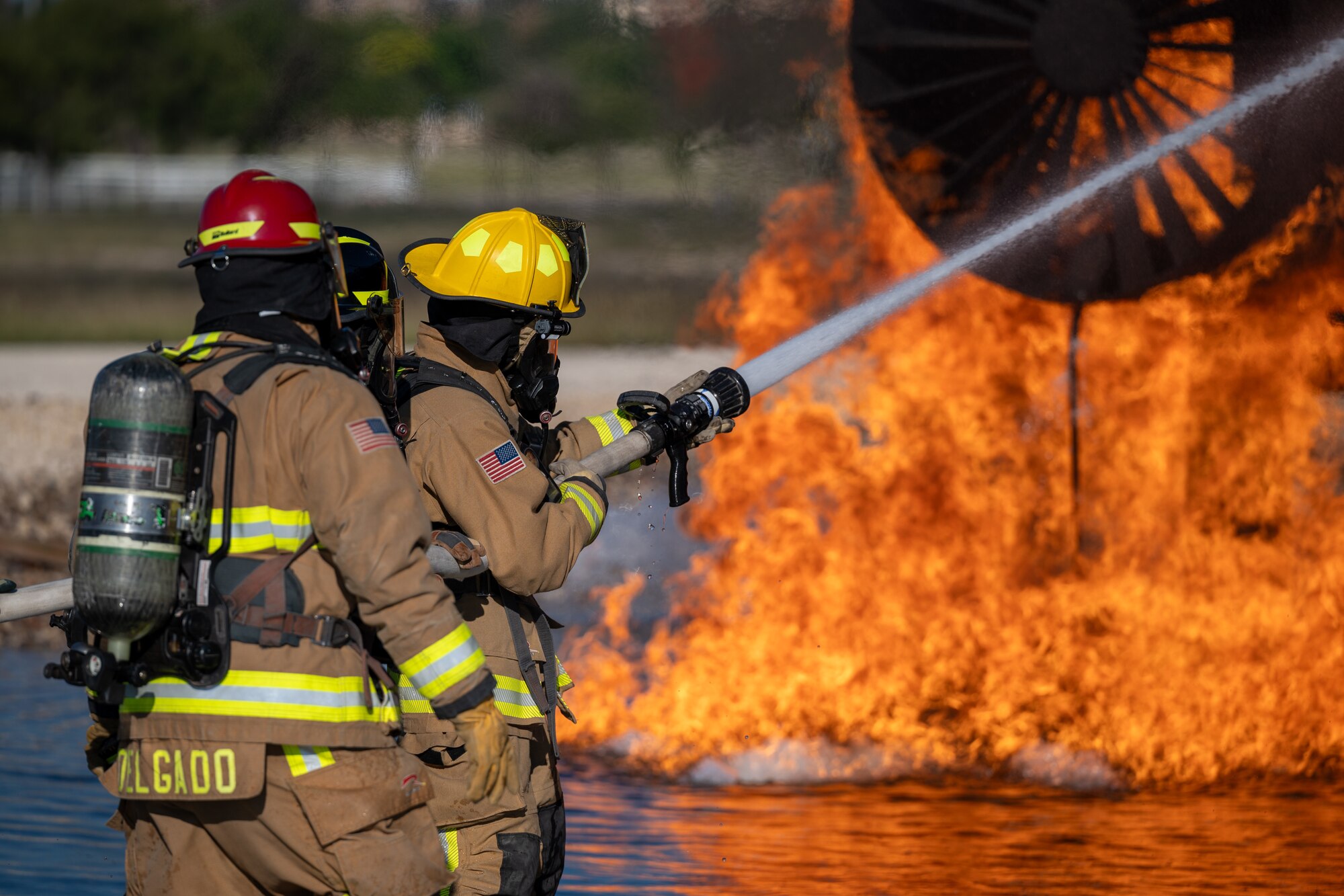 Firefighters from the 47th Civil Engineer Squadron spray water at a simulated engine cell on an aircraft live fire simulator at Laughlin Air Force Base, Texas, Oct. 15, 2024. When fighting the fire, the variable nozzle on the hose will be used to adjust how the stream of water lands on the fire, this can include a large cone of water to a tight jet to blast particular areas. (U.S. Air Force photo by Staff Sgt. Nicholas Larsen)
