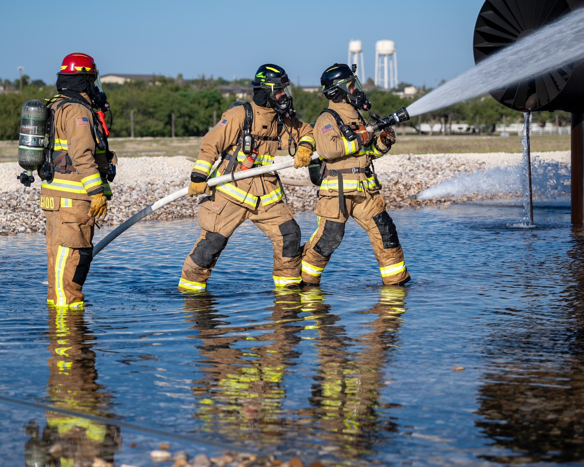 Firefighters from the 47th Civil Engineer Squadron receive additional instructions where to spray water at an aircraft live fire simulator at Laughlin Air Force Base, Texas, Oct. 15, 2024. During the simulation, Firefighters used handlines to apply water to the fire pumping water from the tanker truck. (U.S. Air Force photo by Staff Sgt. Nicholas Larsen)