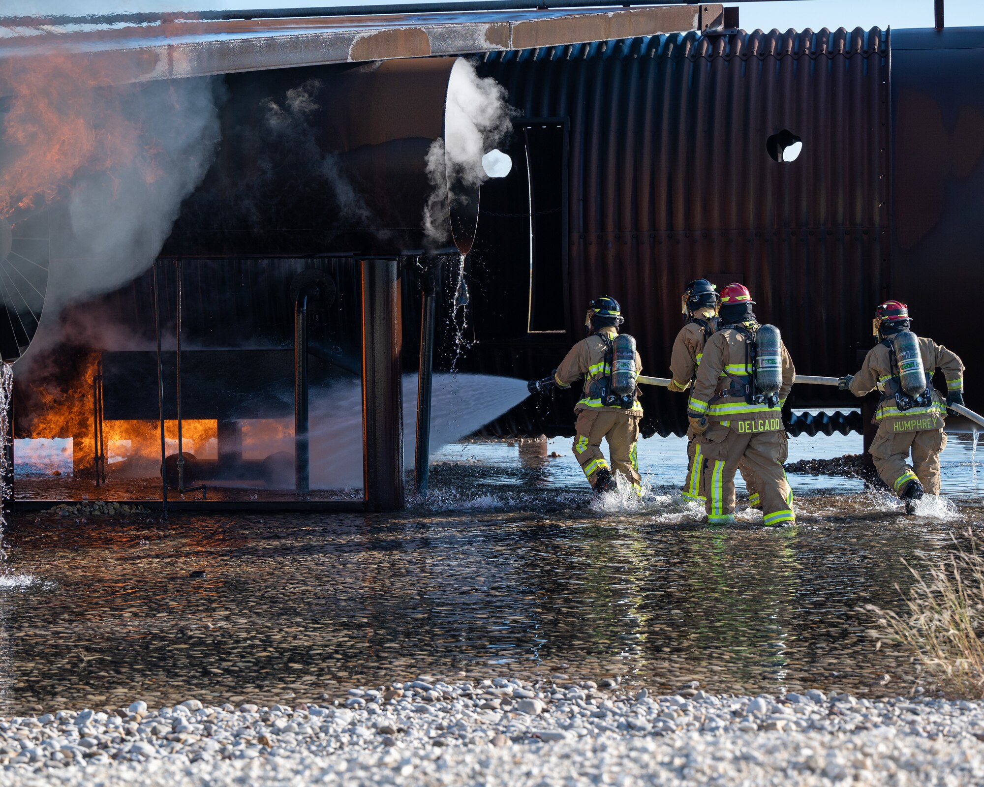 Firefighters from the 47th Civil Engineer Squadron spray water at the base of the fuselage of an aircraft live fire simulator at Laughlin Air Force Base, Texas, Oct. 15, 2024. Live fire simulations are valuable training opportunities for Airmen, allowing them to get advice on approach techniques, the order to put out fires and practice controlling a hose in uneven terrain. (U.S. Air Force photo by Staff Sgt. Nicholas Larsen)