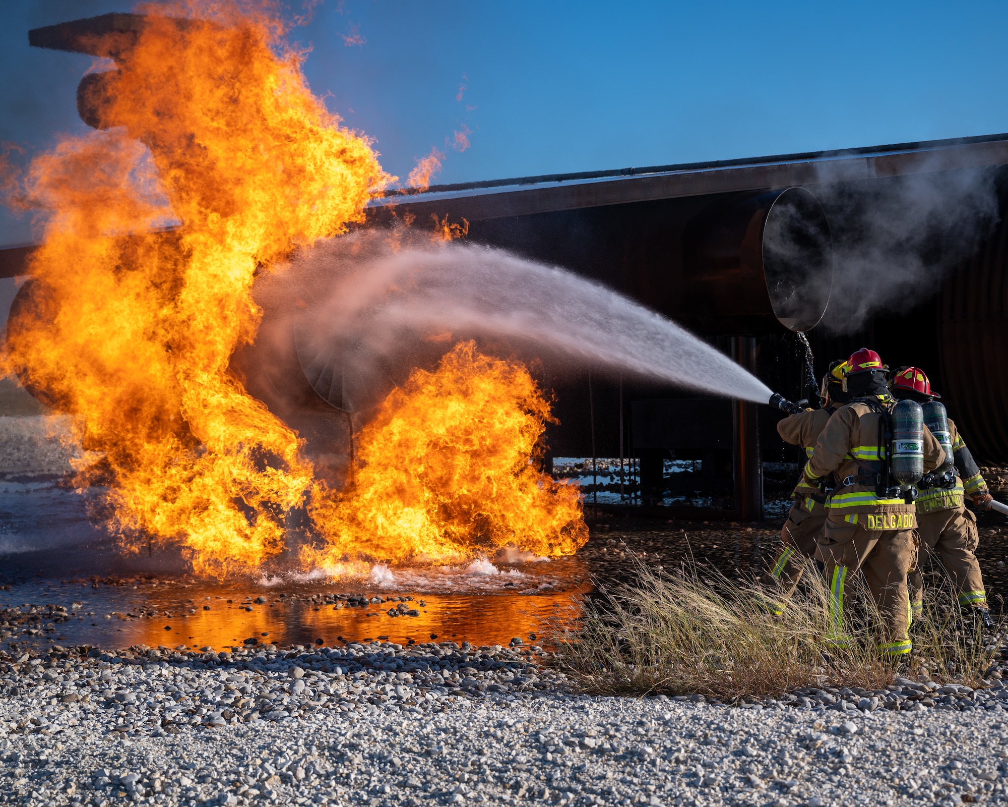 Firefighters from the 47th Civil Engineer Squadron spray water on a simulated engine cell at Laughlin Air Force Base, Texas, Oct. 15, 2024. Live fire simulations are valuable training opportunities for Airmen, allowing them to get advice on approach techniques, the order to put out fires and practice controlling a hose in uneven terrain. (U.S. Air Force photo by Staff Sgt. Nicholas Larsen)