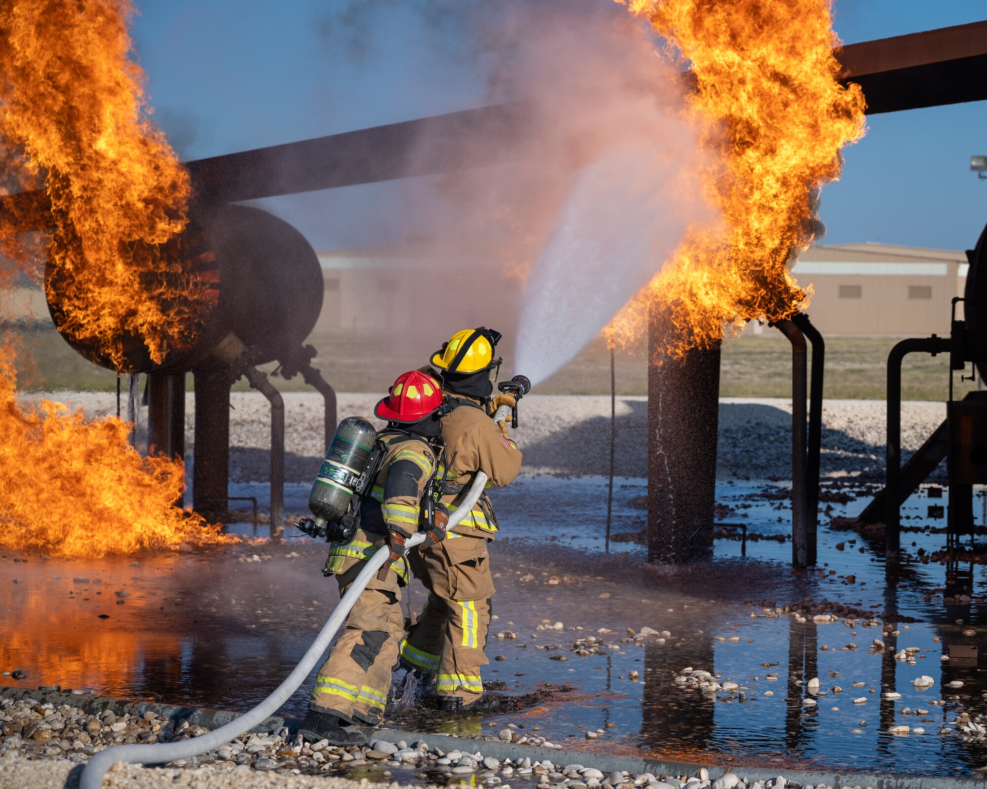 Firefighters from the 47th Civil Engineer Squadron spray water on a simulated engine cell at Laughlin Air Force Base, Texas, Oct. 15, 2024. Live fire simulations are valuable training opportunities for Airmen, allowing them to get advice on approach techniques, the order to put out fires and practice controlling a hose in uneven terrain. (U.S. Air Force photo by Staff Sgt. Nicholas Larsen)