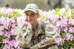 woman in uniform holds crown while posing in front of flowering bushes