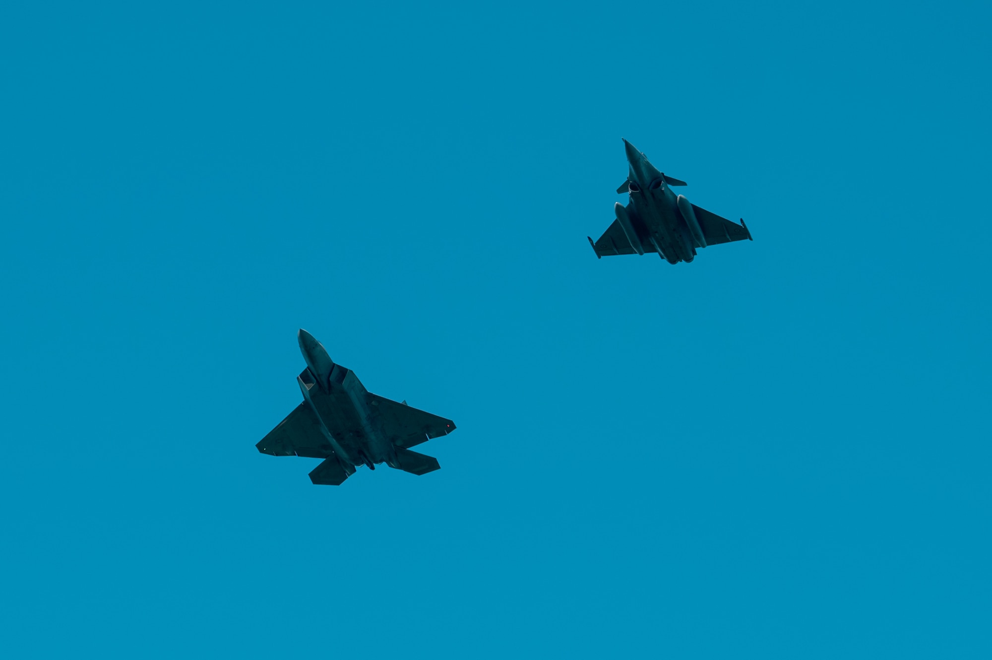 Two fighter jests fly side by side in a clear blue sky.