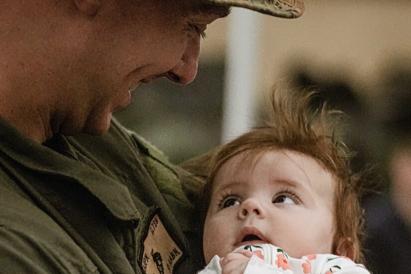 A Marine smiles while holding a baby.