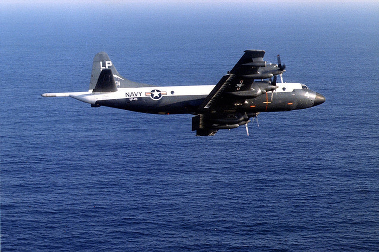 A military aircraft flies over the ocean during daylight.