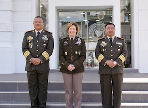 Three uniformed military personnel stand and pose for a photo in front of a building.