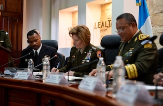 Uniformed military personnel sign an agreement at a table.