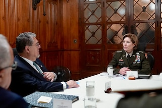 Military personnel and a man in a suit talk at a conference table.