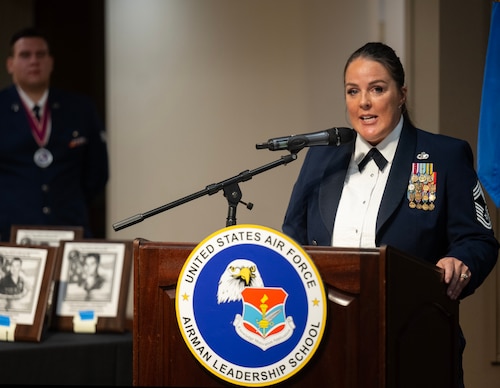 A woman in dress uniform stands at a lectern speaking into a microphone.