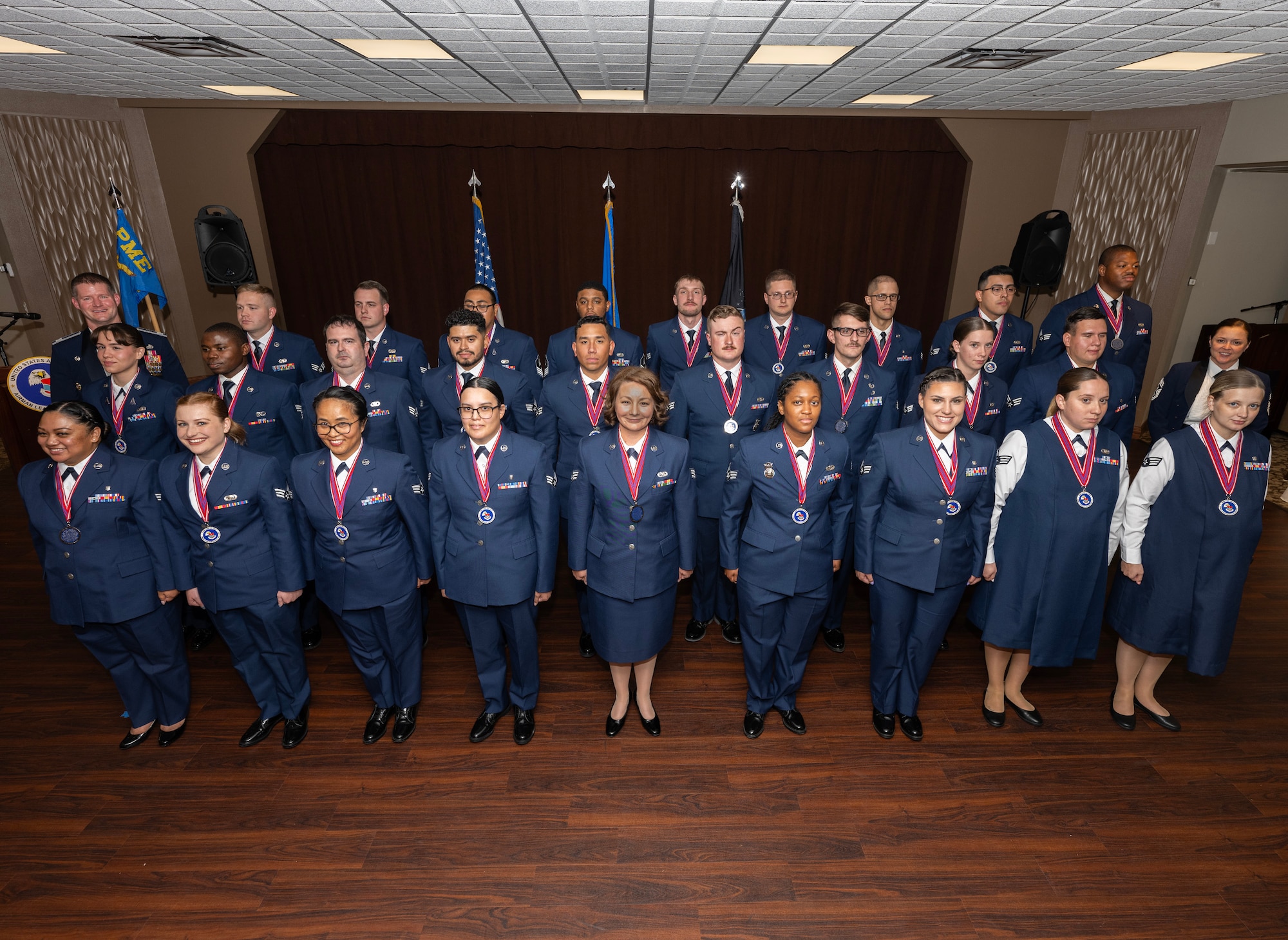 A group of 29 people in dress uniform stand at attention in formation.