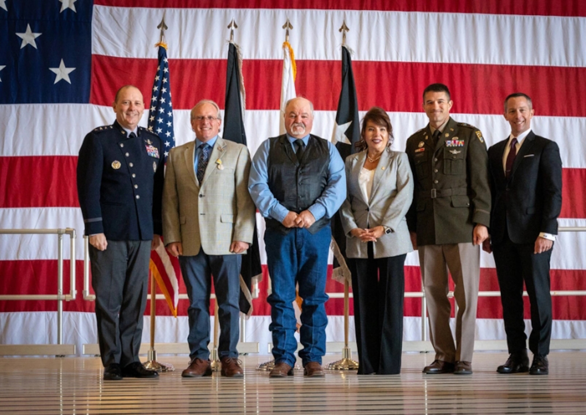 six people pose for a photo on stage in front of a united states flag background