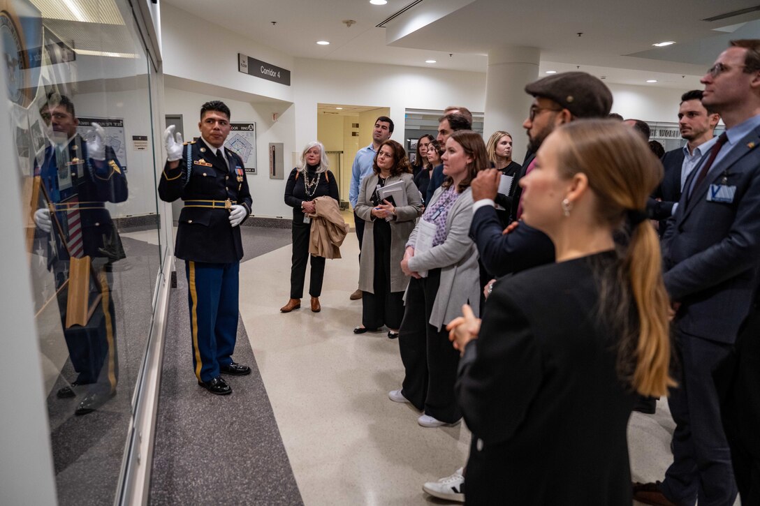 A group of people look at a glass display case as a service member in uniform standing next to it points to it.