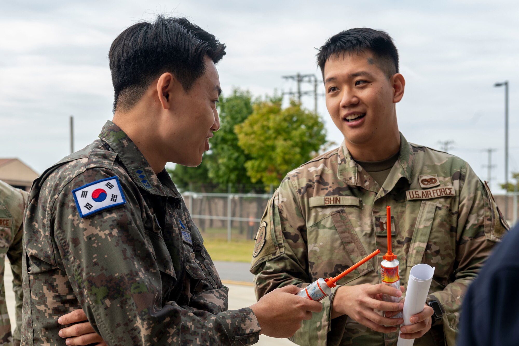 U.S. Air Force Capt. Michael Shin,  36th Fighter Generation Squadron sortie generation flight commander and a Republic of Korea Air Force Airman try tube food during a ROKAF Maintenance Immersion Tour at Osan Air Base, Republic of Korea, Oct. 21, 2024. ROKAF officers were given a tour of the 5th Reconnaissance Squadron where they learned about the U-2 Dragon Lady. (U.S. Air Force photo by Senior Airman Kaitlin Frazier)