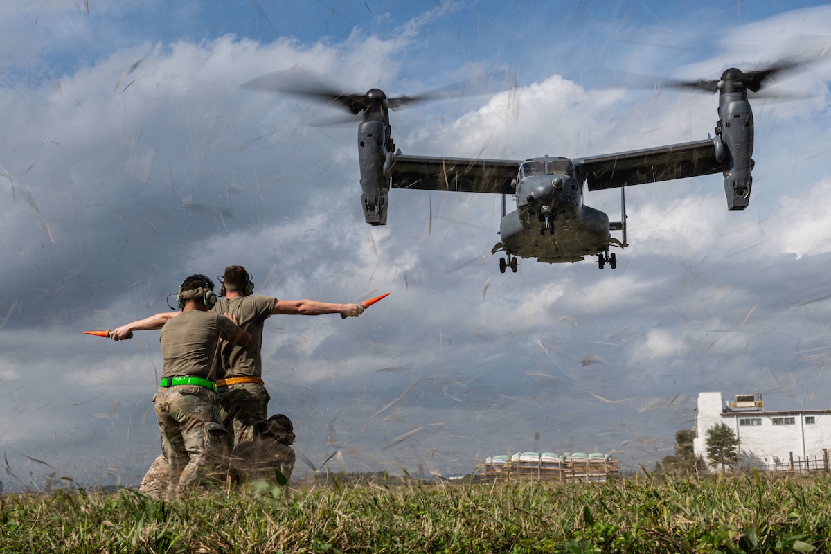 A CV-22 Osprey in flight with people in the foreground