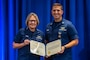 Blue background with Adm. Linda Fagan on the left, Lt. Jordan Hopson on the right, and they are co-holding a decoration.