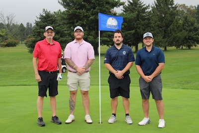 Four golfers stand on a golf course by a flag