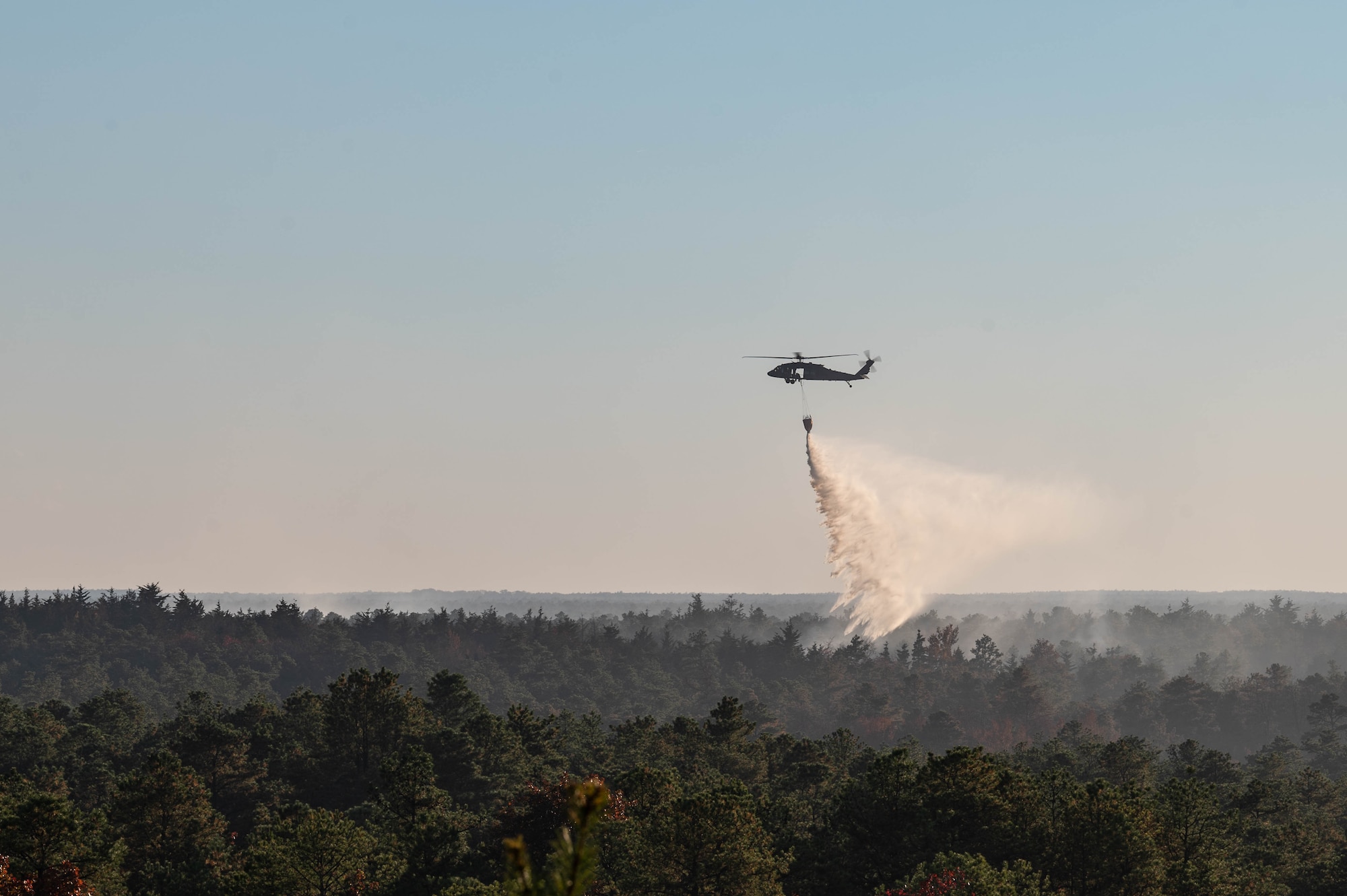 A UH-60 Black Hawk helicopter assigned to 1-150th Attack Helicopter Battalion, performs water drops over a controlled fire on the Joint Base McGuire-Dix-Lakehurst, N.J., range complex at JB MDL, Oct. 23, 2024. The fully contained fire allowed pilots and Joint Base firefighters to train and prepare for fire suppression and disaster response. (U.S. Air Force photo by Senior Airman Aidan Thompson)